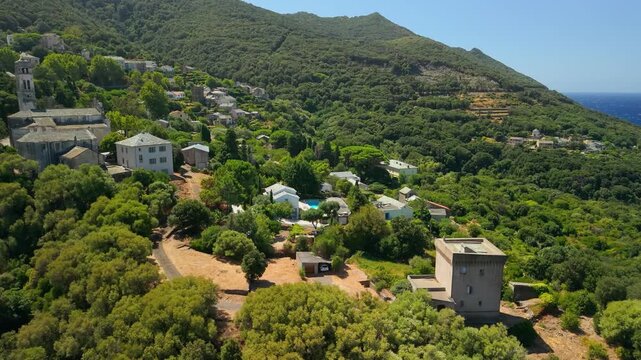 Aerial drone flyover from Pino village to ruined Genoese tower on sea cliff Corsica France. Crashing waves on rocky coast and Mediterranean sea 4K