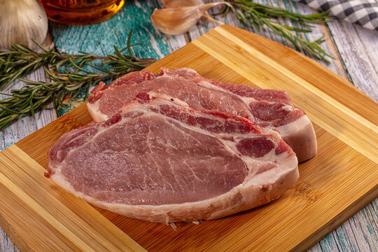 Raw pork chops on bamboo cutting board with rosemary and garlic