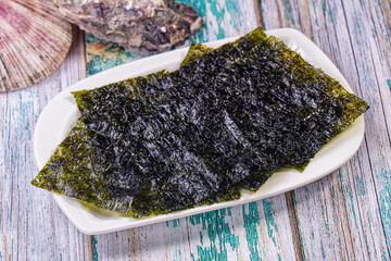 Crispy nori seaweed chips on white plate with seashells on rustic wooden table © Andrei Starostin