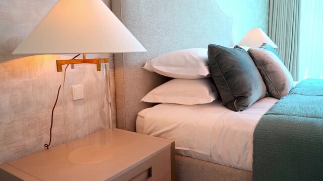 Elegant and modern bedroom interior design featuring a comfortable made bed with plush pillows and a stylish bedside table lamp illuminating the room. Perfect for real estate and hospitality concepts