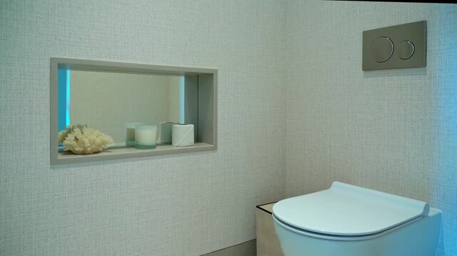 Sleek, modern toilet room featuring a wall hung commode and a recessed wall niche with decorative items, illuminated by changing ambient light for a contemporary and luxurious feel