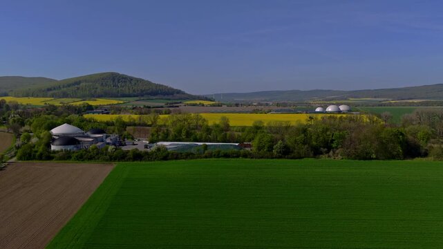 Aerial video revealing multiple biogas plants surrounded by extensive agricultural fields and rolling countryside in Germany during spring.