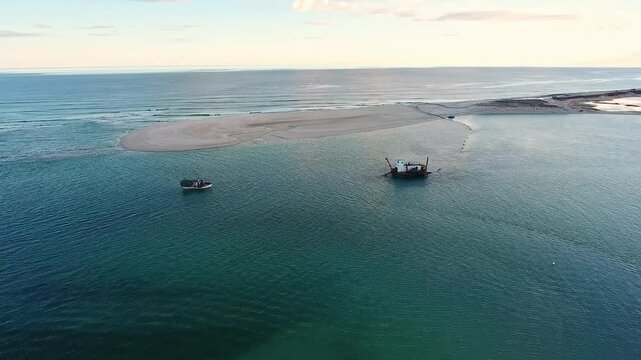 Aerial view of a dredger extracting sand from the seabed near a small fishing boat in the beautiful calm waters of the ria formosa natural park in fuseta, algarve, portugal