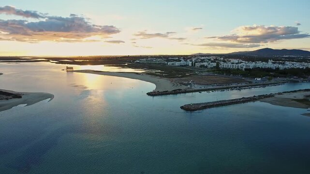 Stunning aerial perspective showing the sunset over the beautiful ria formosa lagoon, featuring fuseta beach and the town of tavira with calm waters reflecting the golden sky in algarve, portugal