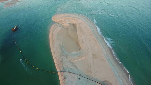 Stunning aerial footage capturing a dredging operation working to replenish a beautiful sandy beach, with a long pipe transferring sand from the turquoise sea to the shoreline in portugal