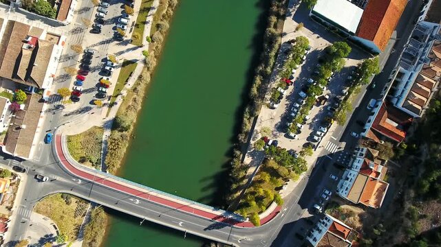 Aerial drone flying over the ancient roman bridge crossing the gilao river in tavira, portugal, capturing the urban landscape, car traffic, and parking lots along the riverbanks