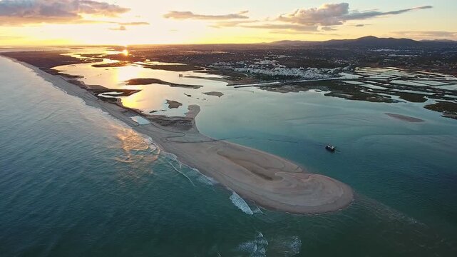 Golden sunset light reflecting on the calm waters of the ria formosa lagoon in portugal's algarve region, with an aerial view of a sand dredging ship operating near the coast