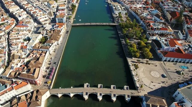 Stunning aerial perspective slowly flying over the historic cityscape of tavira, featuring the ancient roman bridge crossing the serene gilao river in the beautiful algarve region of portugal