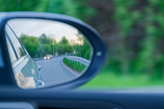 View of a winding road and car headlights reflected in a vehicle side mirror