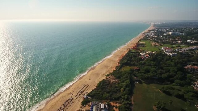 Sunny aerial drone view flying along the beautiful coastline of garrao beach in vale de lobo, algarve, portugal, with calm turquoise ocean waves gently lapping onto the golden sandy shore