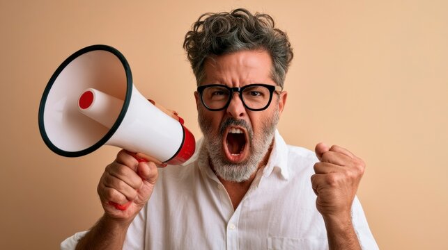 Angry middle-aged man with glasses shouting through a megaphone with a clenched fist in a studio portrait