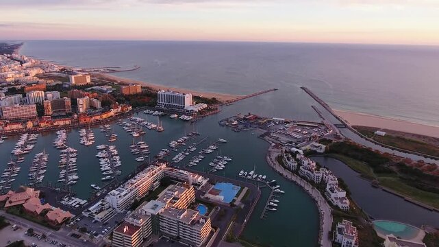 Dramatic aerial view of vilamoura marina in the algarve region of portugal, showing boats and yachts docked in the harbor as the sun sets over the beautiful atlantic coastline