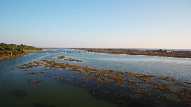 Majestic aerial view flying over the iconic wooden footbridge at quinta do lago, traversing the beautiful ria formosa lagoon towards the atlantic ocean coast during a tranquil sunset