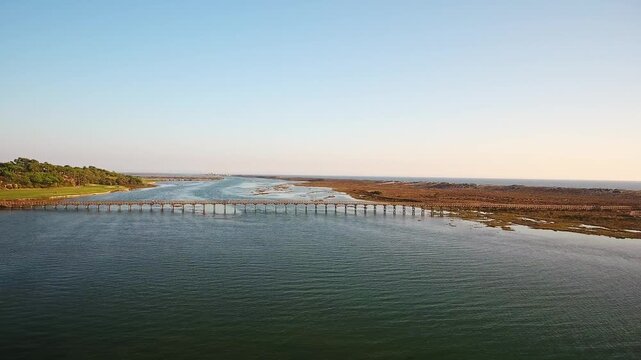 Beautiful aerial perspective moving towards the iconic wooden footbridge at quinta do lago, crossing the ria formosa lagoon towards the atlantic ocean during a stunning golden hour sunset
