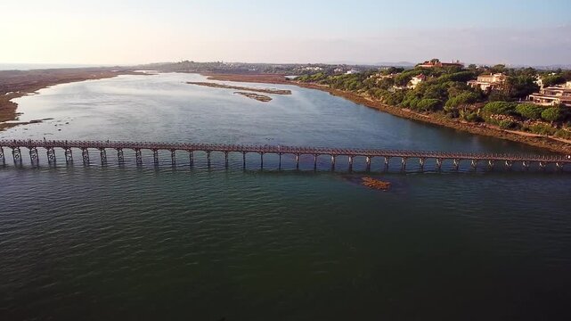 Drone footage panning sideways over the iconic wooden pedestrian bridge crossing the ria formosa lagoon in quinta do lago, algarve, a popular tourist destination in southern portugal at sunset