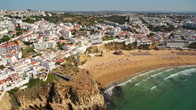 Sunny aerial perspective of the stunning albufeira coastline, showing the famous fishermen's beach crowded with tourists alongside the charming white washed buildings of the historic old town