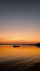 Obraz premium Serene ocean sunrise with golden water reflections and distant boat in vertical view