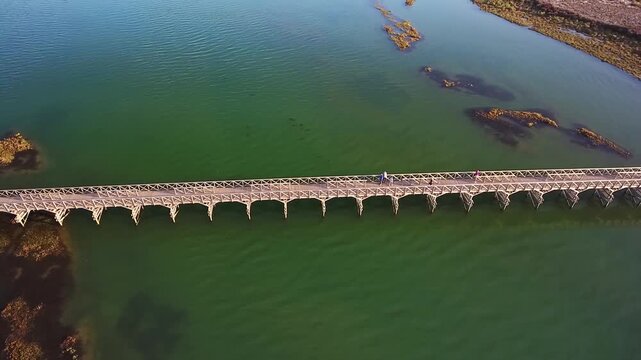 Aerial top down view of people walking along the iconic wooden footbridge at quinta do lago in the algarve region of portugal, a famous landmark connecting to a golf course and beach