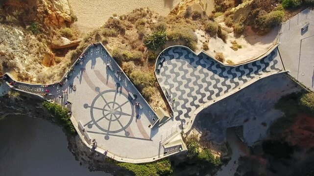 Aerial view of miradouro dos tres castelos in portimao, algarve, showing traditional calcada pavement, tourists on the cliffside promenade and sunlit coastal seascape