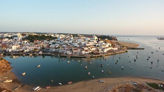 Aerial perspective of the traditional portuguese fishing village of ferragudo in the algarve, showing its whitewashed houses and the arade river estuary filled with boats at sunset