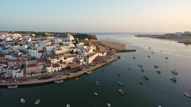 Beautiful aerial view of the fishing village of ferragudo in the algarve, portugal, overlooking the arade river with boats and yachts anchored at sunset during golden hour