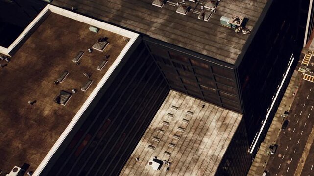 Aerial view showing city rooftops with various structures. People are on one of the rooftops. Equipment is placed on the buildings. This scene captures urban life from above.