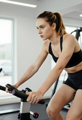 Fototapeta premium Fitness and wellness motivation, young woman training on stationary bike in gym for cardiovascular health and weight loss goals in modern sports club