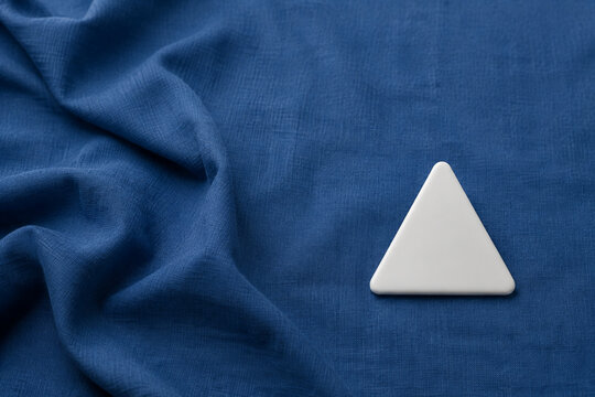 Single white equilateral triangle object on deep blue linen, calm still life for editorial concept