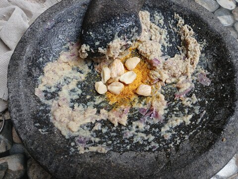 Freshly ground herbs and spices in a traditional stone mortar and pestle (cobek dan ulekan) for authentic Indonesian cooking preparation