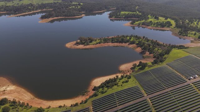 Christmas Hills, Australia - 31 August 2026: Aerial view of Sugarloaf Reservoir with rows of solar panels in the foreground and surrounding green hills.