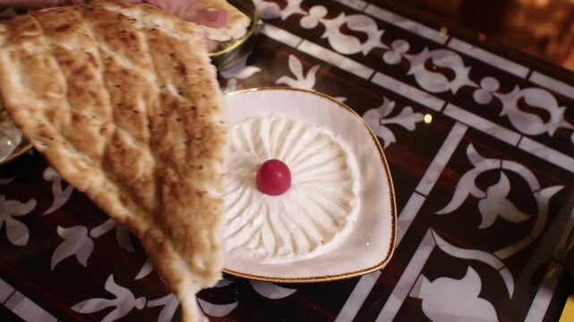 Person tearing freshly baked flatbread to eat with a traditional Middle Eastern appetizer