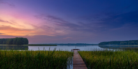 Tranquil Sunset Over Lake with Wooden Pier and Reeds Landscape
