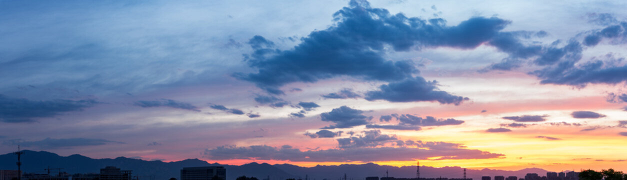 A serene twilight scene showing colorful sunset sky, scattered clouds, distant mountain ranges, and faint urban silhouettes on the horizon.