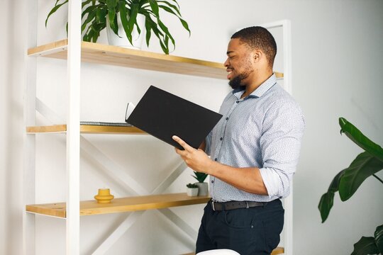 Black male entrepreneur standing in office near bookshelf and holding documents