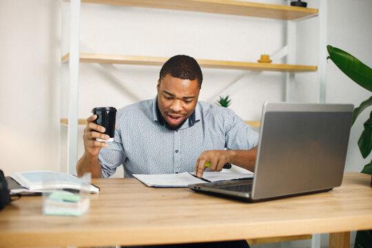 Black male entrepreneur sitting in office, using laptop and drinking coffee