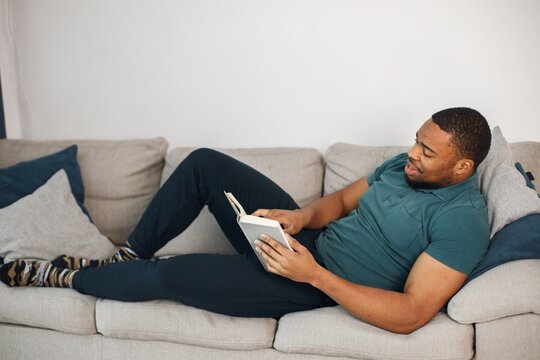 Black guy lay on a couch in living room with a book