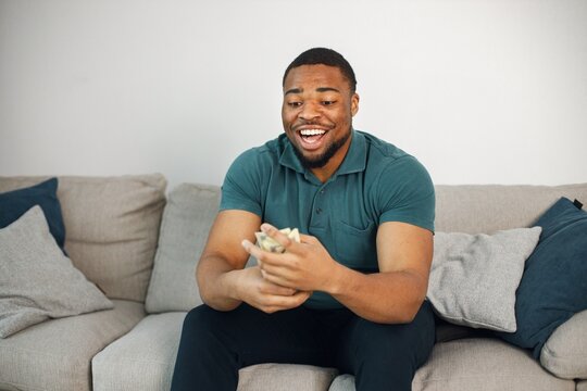 Black guy sitting on a couch in living room holding a cash