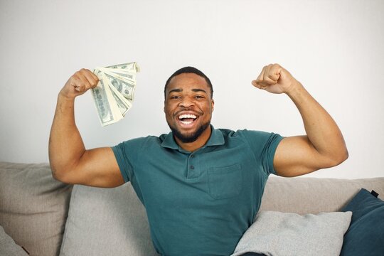 Black guy sitting on a couch in living room holding a cash