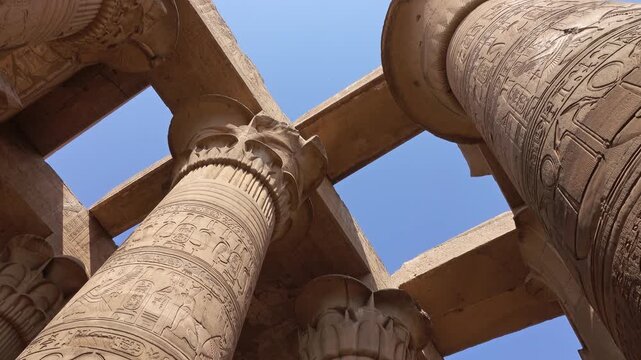 View of the ancient Temple of Kom Ombo with intricate hieroglyphic carvings on stone columns under a clear blue sky in Aswan, Aswan Governorate, Egypt.