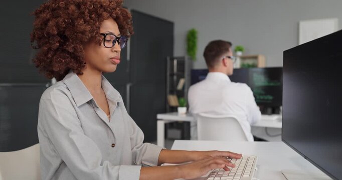 Programmer developer woman coding at computer office. She types at a monitor with code while a coworker nearby signals productivity and a modern IT workspace. Clear concept of software teamwork.