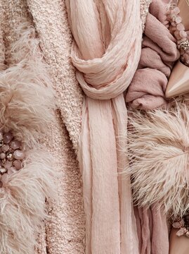 Flat lay of various accessories and items arranged on a beige background. on the left side of the image, there is a close-up of a pink scarf tied in a knot.