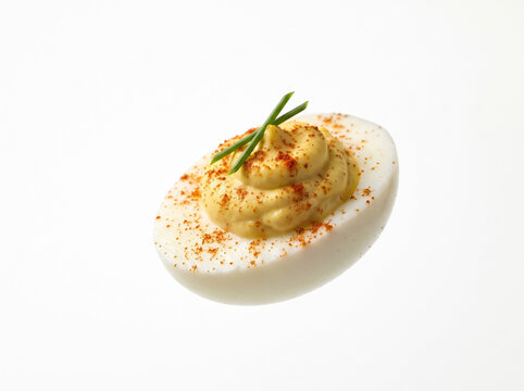Deviled egg garnished with paprika and chives on white background