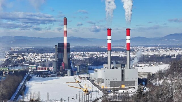 Wildon, Styria, Austria - 29 March 2026: Aerial view of Kraftwerk Wildon power plant with smoking chimneys in a snowy landscape.