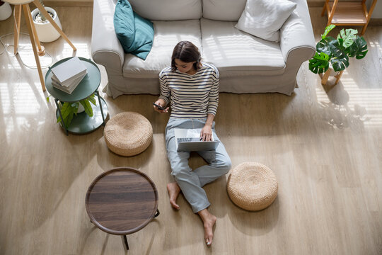 Asian Woman Using Smartphone and Laptop While Relaxing on Sofa at Home
