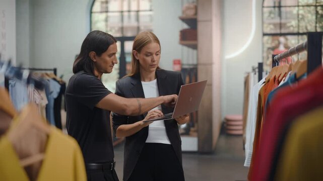Clothing Store Shopping. Teamwork as a Female Shop Manager Holds a Laptop, talks to Sales Area While a Male Sales Associate Studies the Screen, Discussing Display Plans, Product Placement. Static Shot