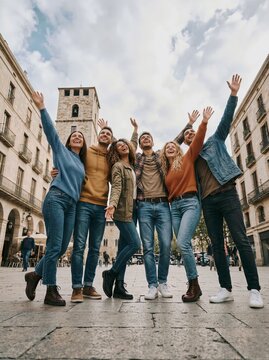 Diverse group of young friends celebrating together in city square with raised arms