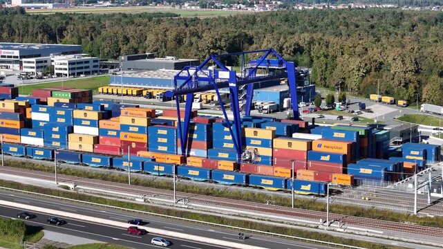 Werndorf, Steiermark, Austria - 19 September 2025: Aerial view of Cargo Center Graz with colorful shipping containers, blue gantry crane, railway tracks, and trucks.