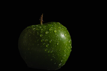 Fresh green apple covered with water droplets, isolated against a black background, highlighting natural texture, freshness and healthy food concept. © yusuf