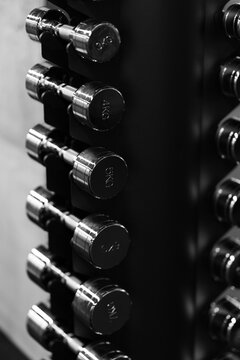 Close up of chrome dumbbells on a black weight rack in a modern gym, highlighting strength training equipment with dramatic monochrome contrast.