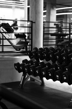Black and white dumbbell rack in a modern gym, featuring strength training equipment, industrial interior details and dramatic high contrast lighting.